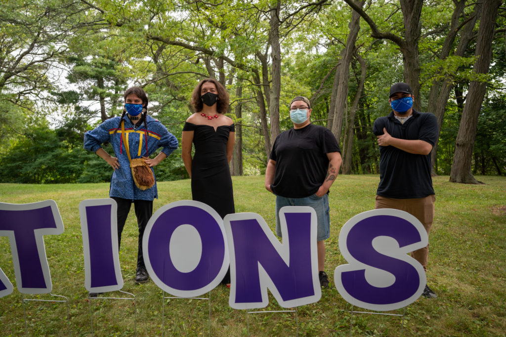 Four people stand outside behind a congratulations sign.