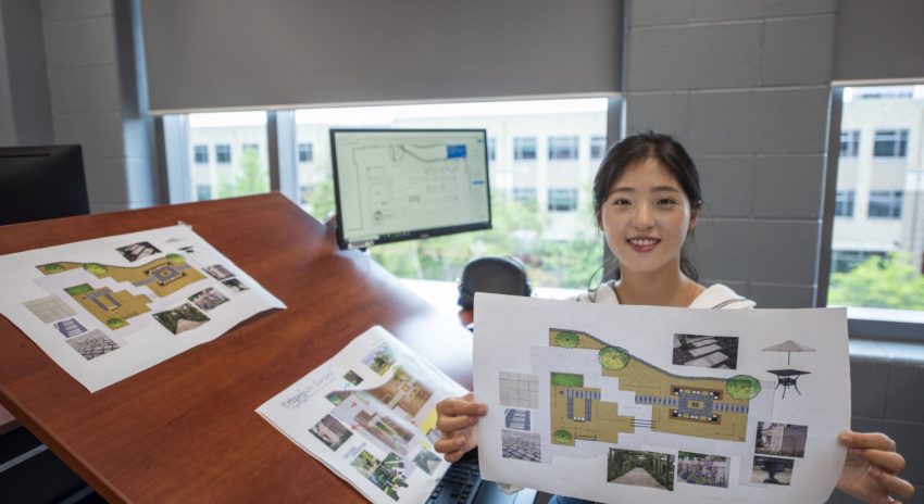 a student holds up her design plans for a garden
