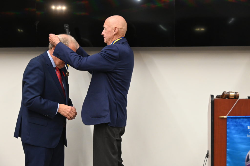 a bald man in a suit places a medal around the neck of a man wearing a blue suit and red tie
