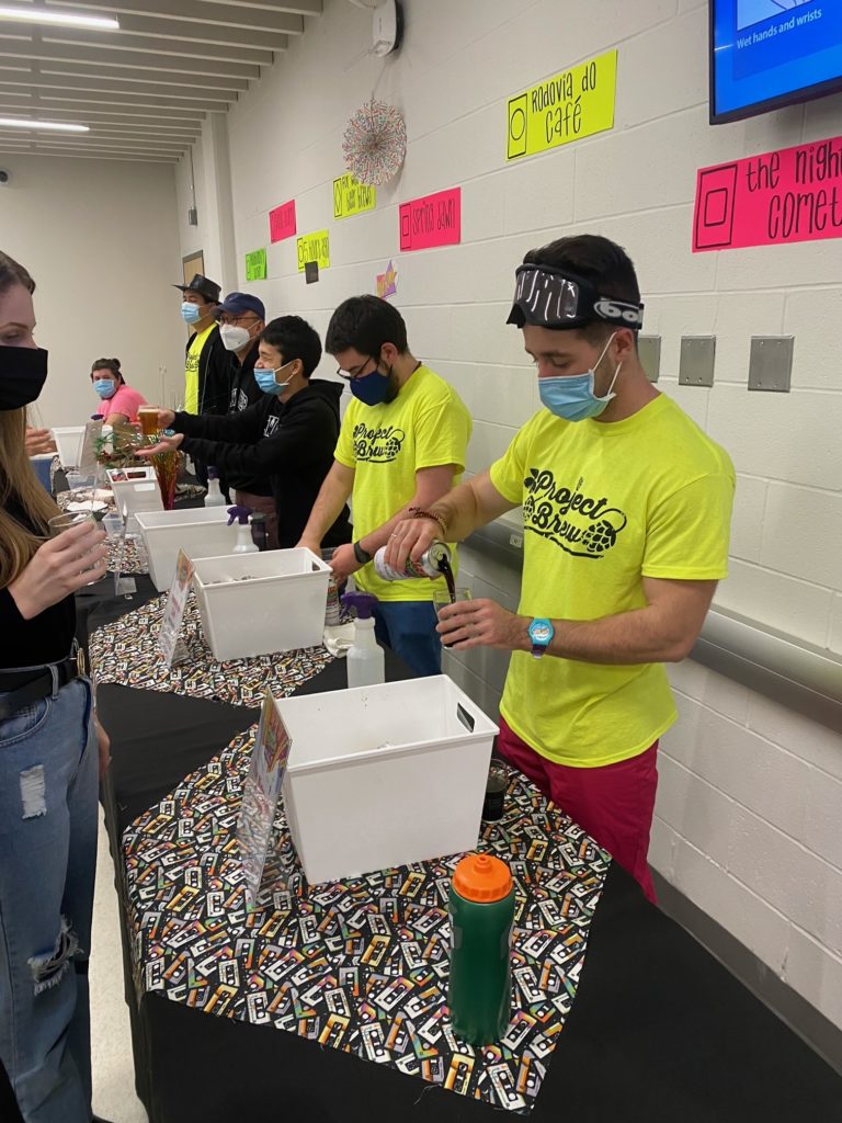 A group of students wearing neon yellow shirts pour beer for guests at Project Brew