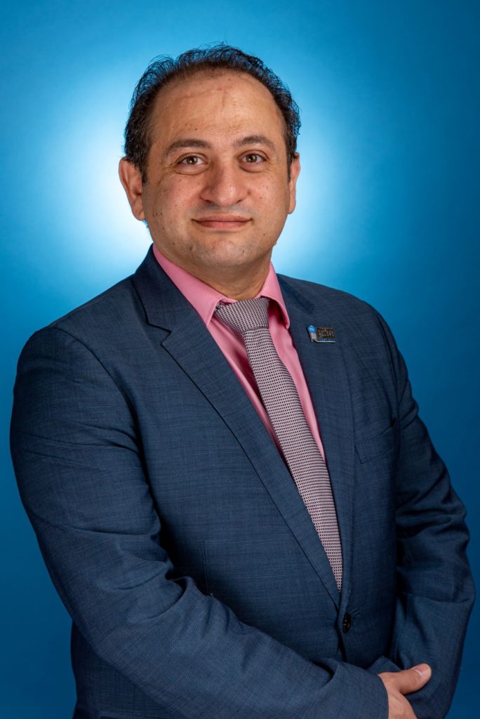A man wearing a blue suit smiles at the camera