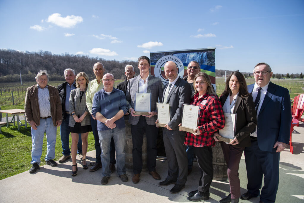 a group of people standing side by side with the Niagara escarpment and NC vineyards in the background