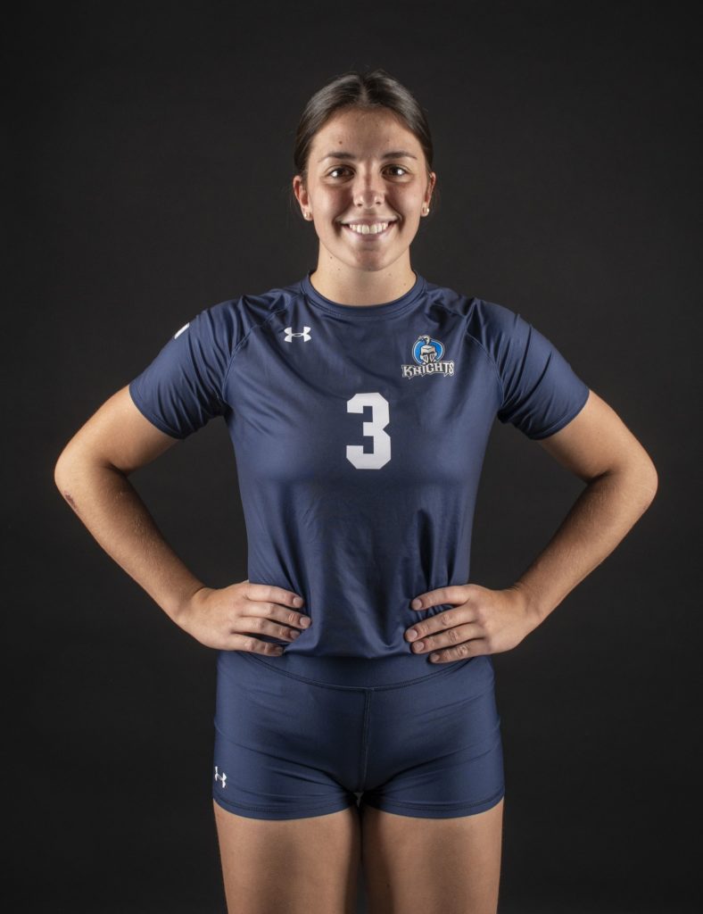 a female volleyball player in uniform smiles at the camera