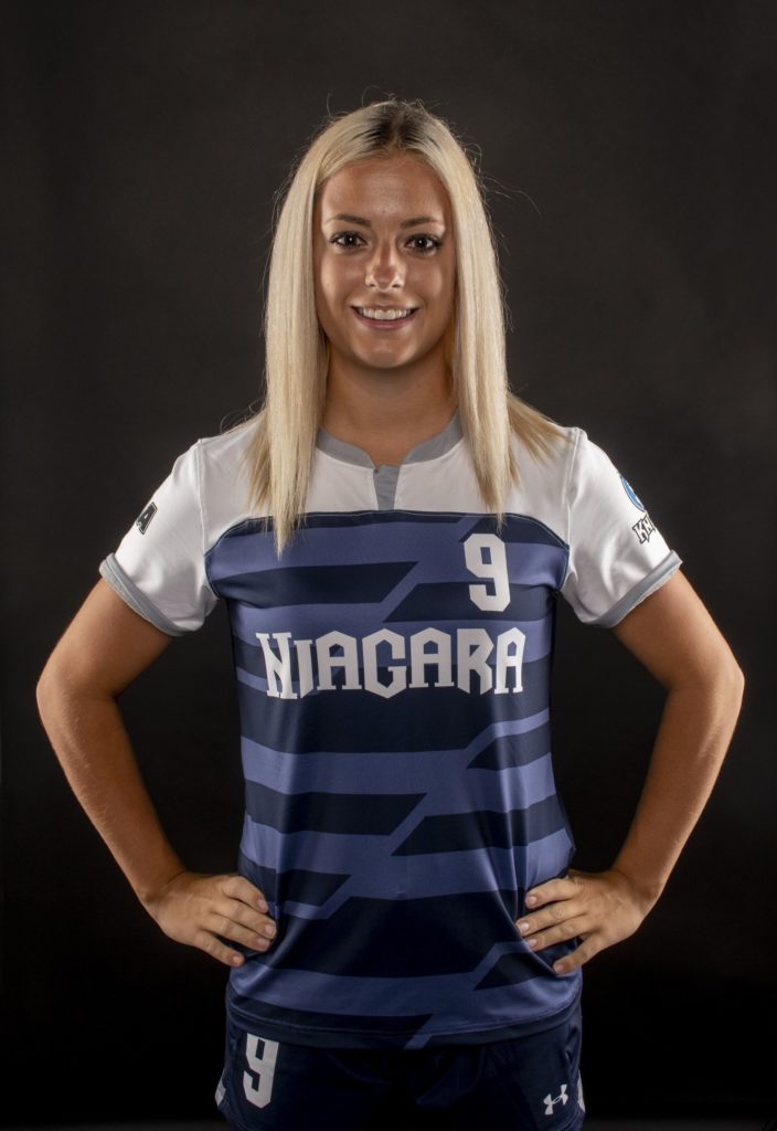 a female student athlete wearing a soccer uniform smiles at the camera