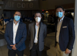 three men wearing face masks and blazers stand side by side for a photo