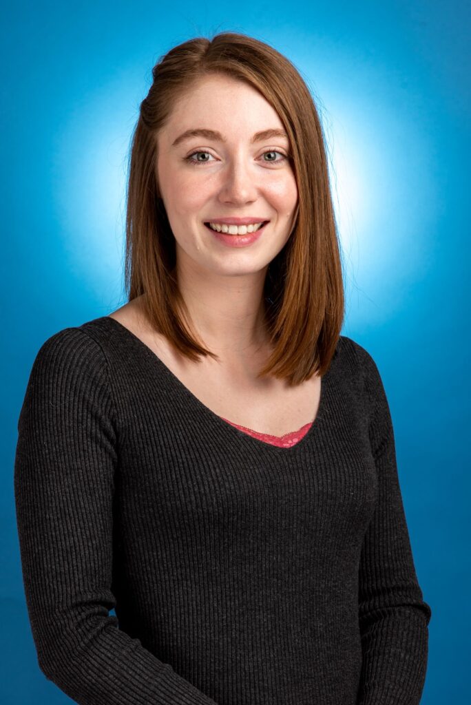 a woman with shoulder length brown hair wearing a black sweater smiles at the camera