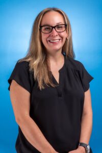 a woman with long blonde hair wearing glasses and a black blouse smiles at the camera