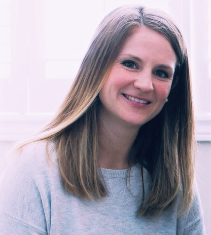 a woman with long hair wearing a grey sweater smiles at the camera