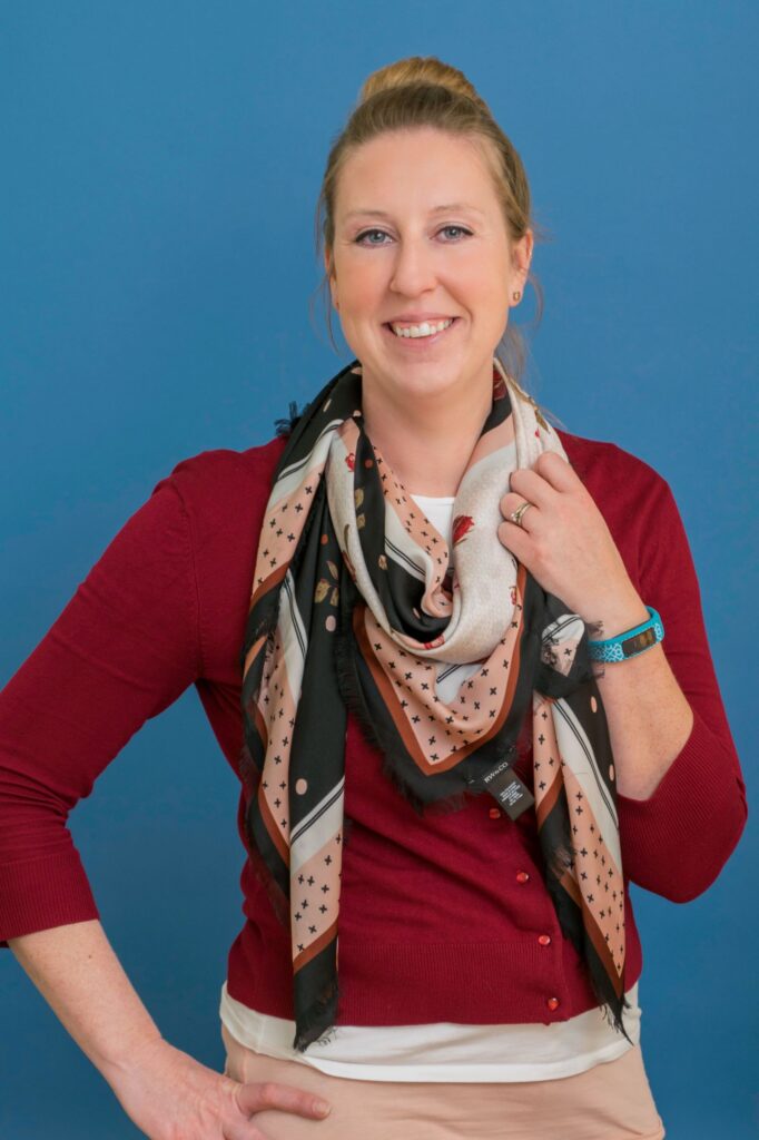a woman wearing a red sweater and colourful scarf smiles at the camera