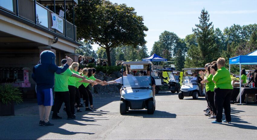 volunteers cheer golfers riding in a golf cart