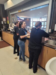 three women stand at a counter preparing food