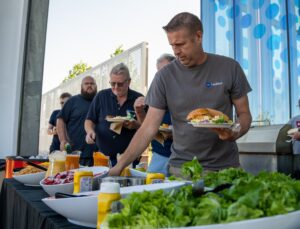 Five people walk along a buffet table collecting food items for their plates.
