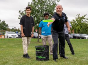 Three men watch as a fourth throws a Frisbee