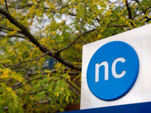 The NC button logo on an outdoor sign with fall foliage in the background
