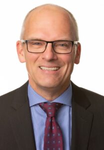 A headshot of a man wearing glasses, a suit jacket and tie.
