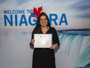A girl with glasses standing while smiling at camera and holding award.