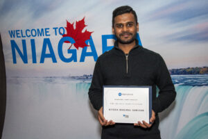 A man in a black shirt standing and looking at camera while holding an award.