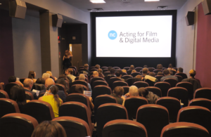 Inside of a small movie theatre with the words Acting for Film & Digital Media on the screen