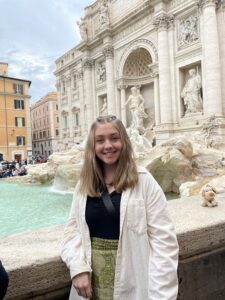 A girl standing in front of a statue and fountain in Italy.