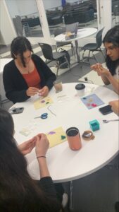 a group of women create beaded bracelets around a small table