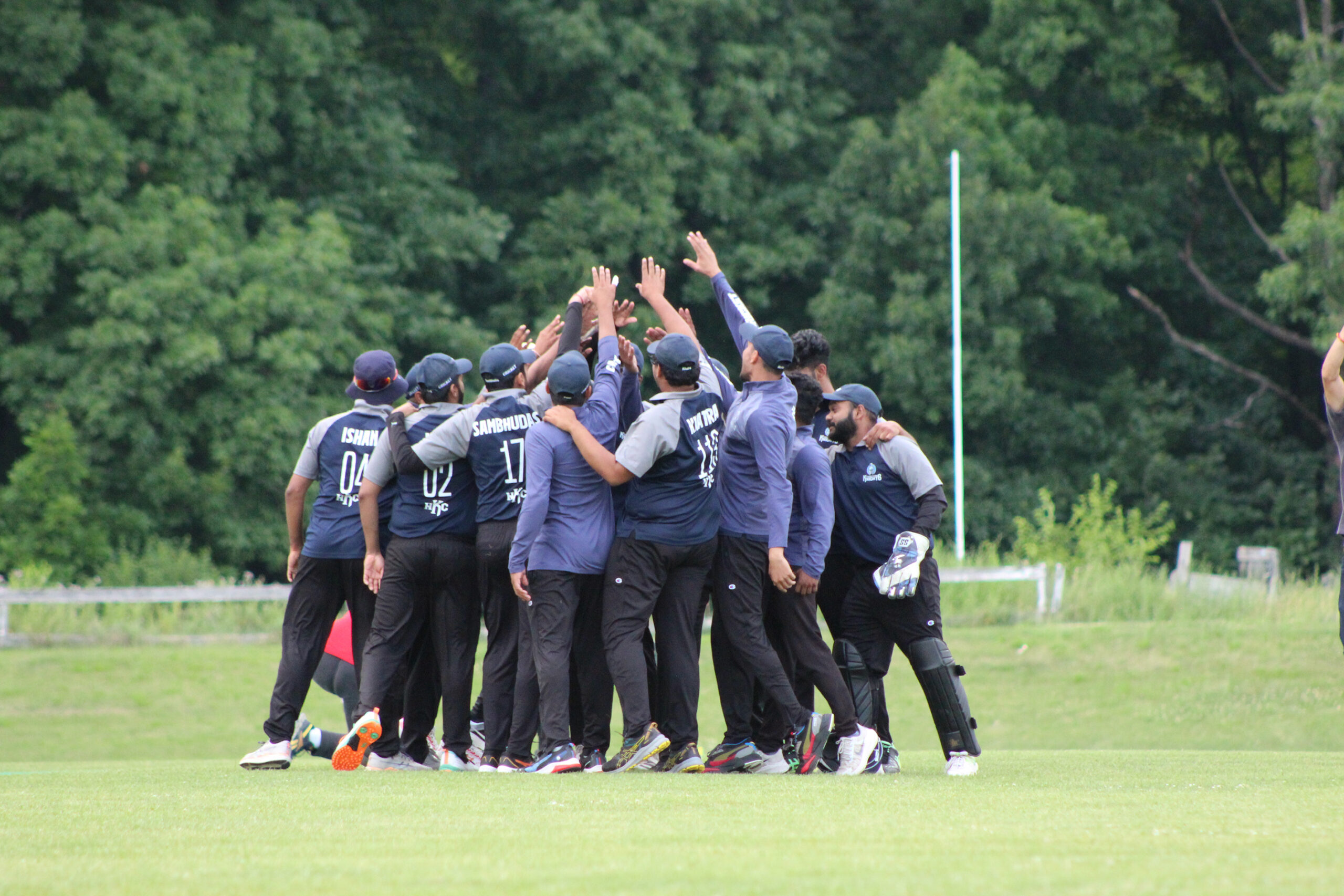 a team of cricket players gather in a huddle with hands in air