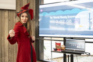 A woman dressed as a red witch standing in front of screen.
