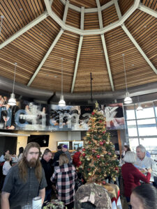 People gathered in indoor dining space with Christmas tree in the centre.