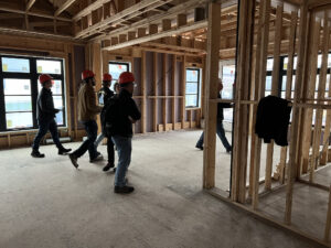A group of people walking through house construction site with wood wall panels.