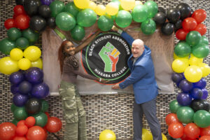 Two people posing in front of a balloon arch with their hands displaying around a circular logo.