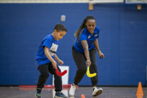a student plays hand hockey with a child in a gym