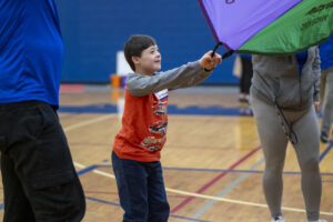 a smiling child hold onto a large parachute in a gym