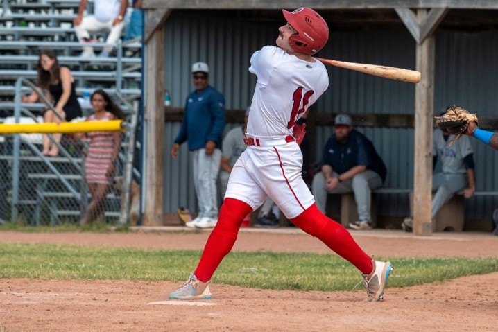 Baseball player on the field swinging bat wearing red and white.