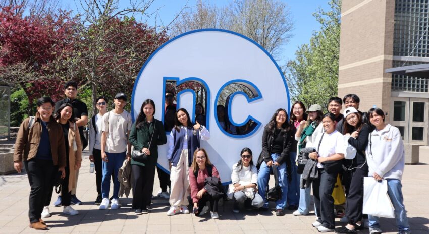 a group of people pose outside in front of a large NC circle on campus