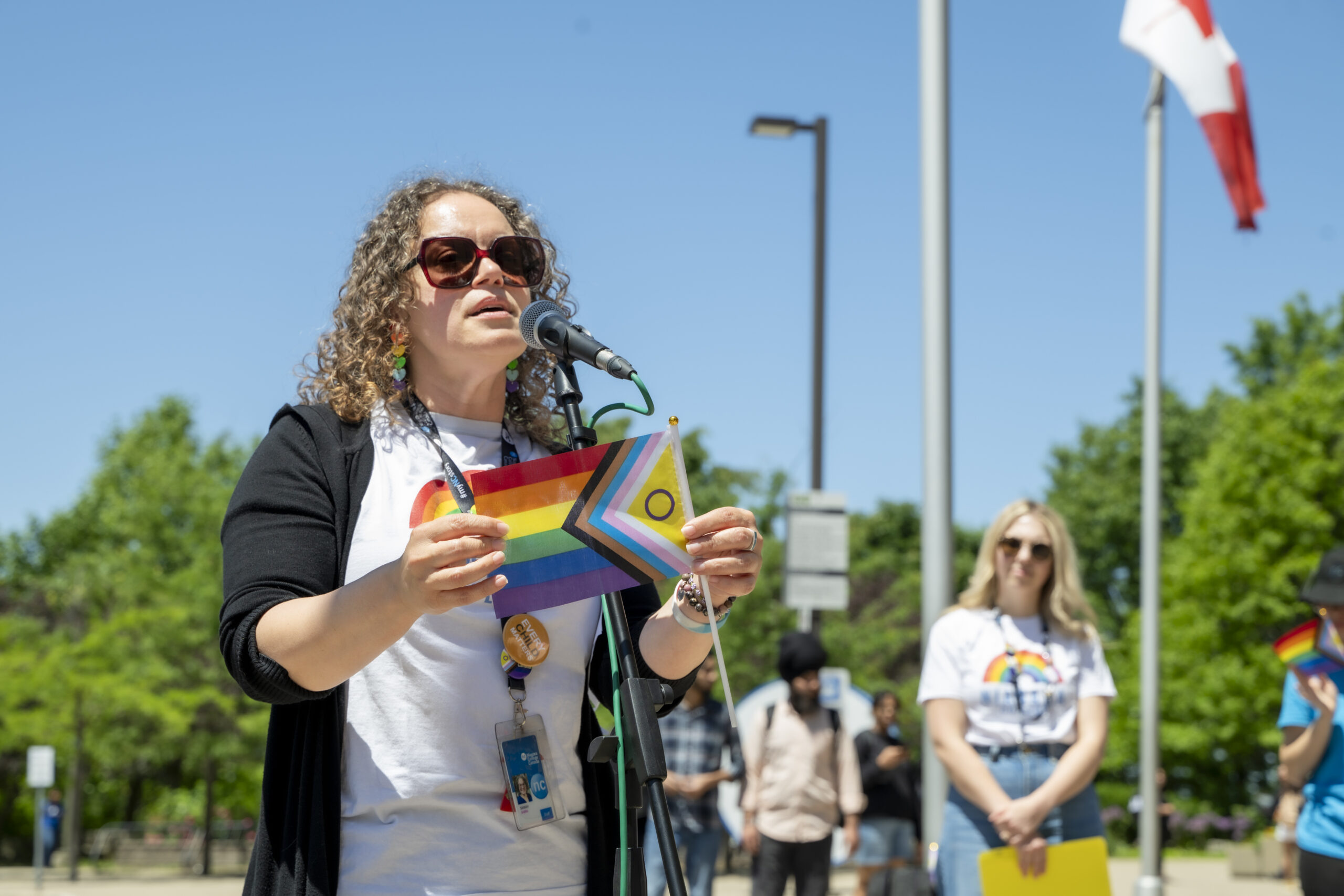 Women stands at mic stand holding the progress pride flag.