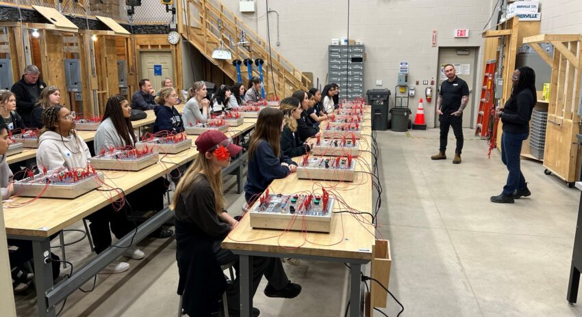 two rows of students sitting in an electrical lab looking at a women speaking