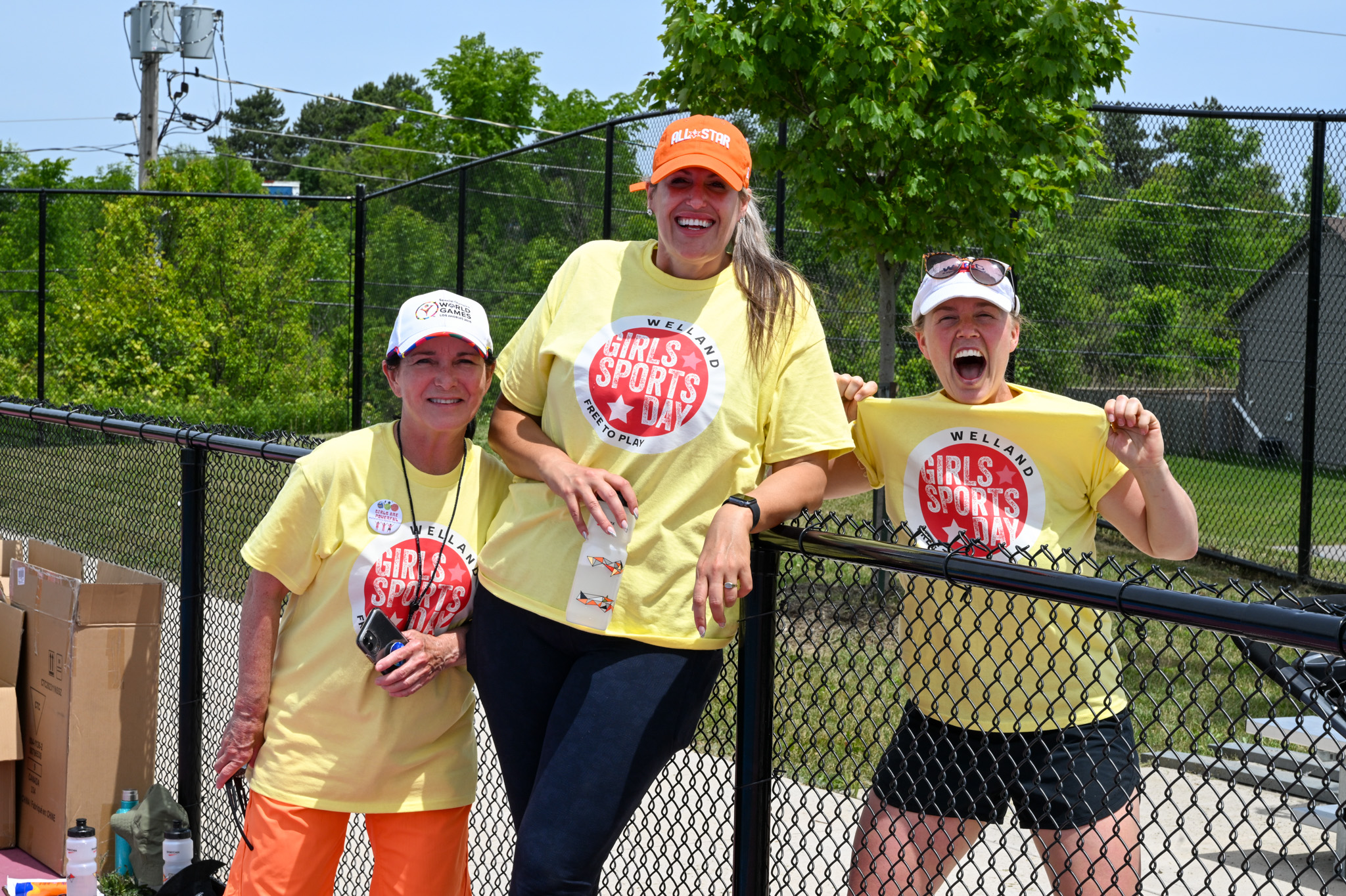 three women stand together by a black fence
