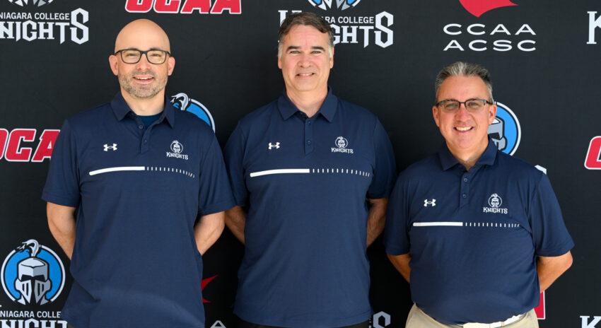 Three male coaches wearing blue NC Knights polo shirts pose for a photo