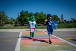 two mascots - a turtle and a Knight - walk through a rainbow crosswalk