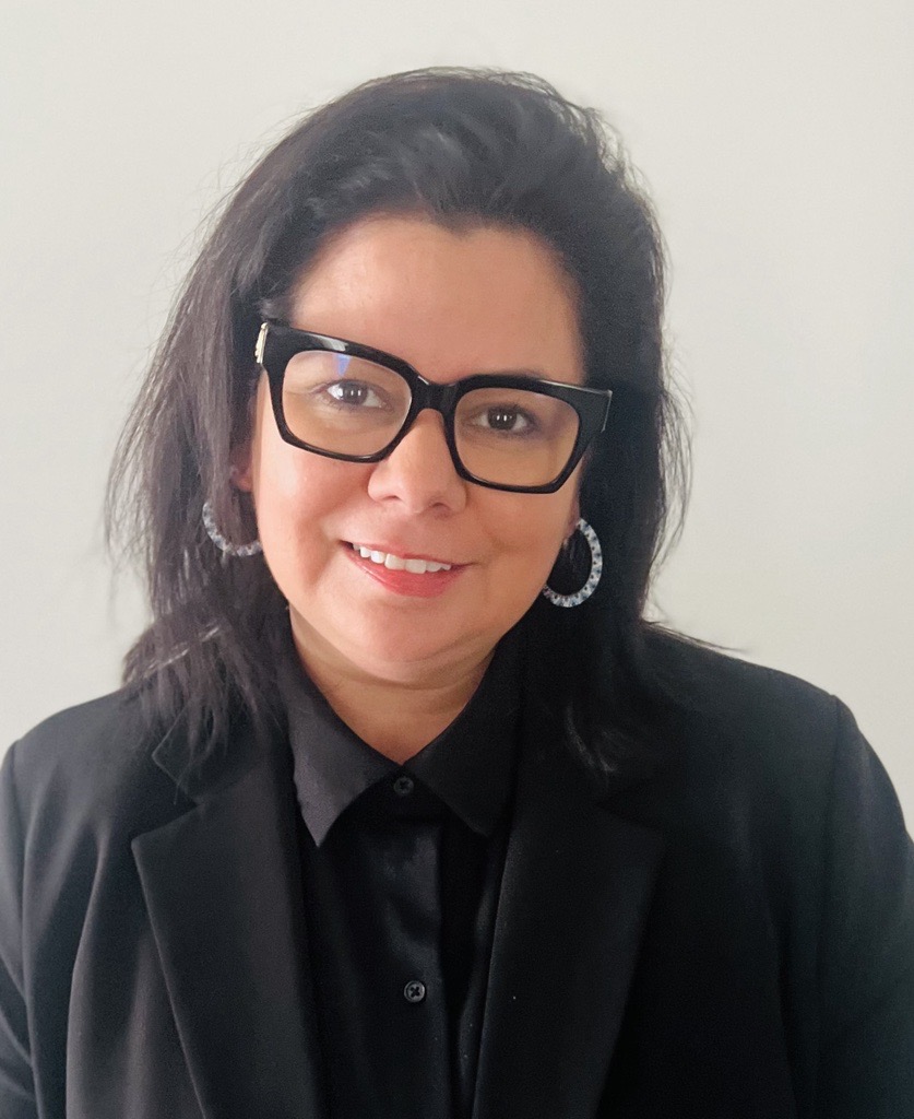a woman with dark hair and black glasses smiles for the camera