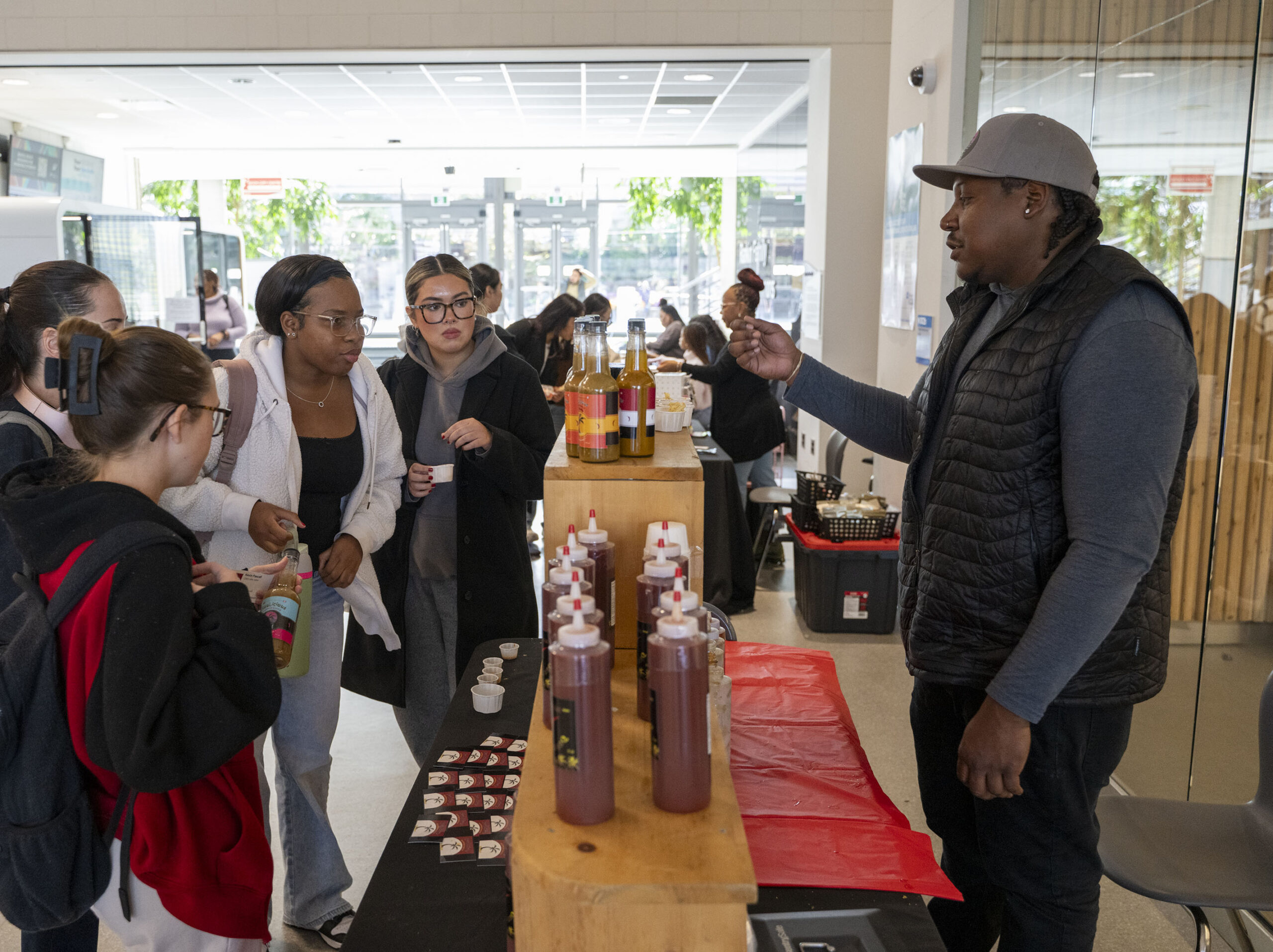 a group of female students sample hot sauce and barbeque sauces at a vendor fair