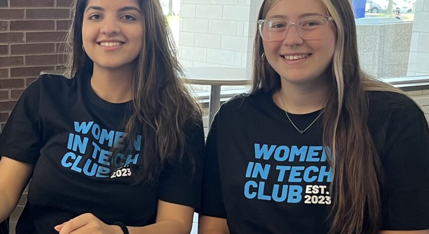 two young women wearing black and blue t-shirts sit at a table