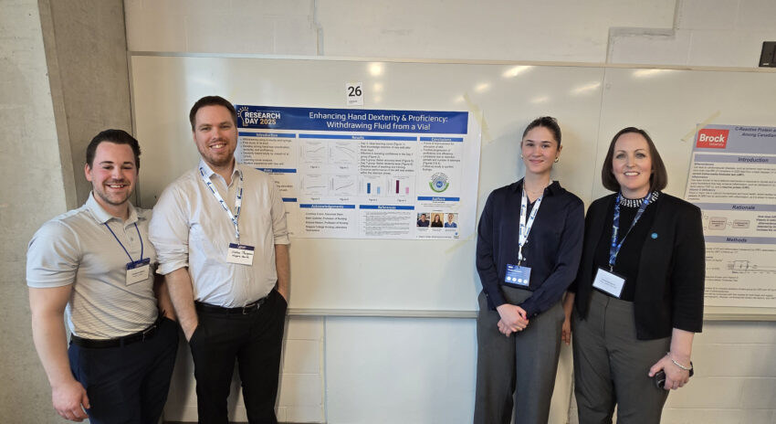 four people stand in a classroom in front of a large poster taped to a white board