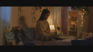 a screenshot of a movie scene featuring a young woman in her bedroom sitting on her bed reading