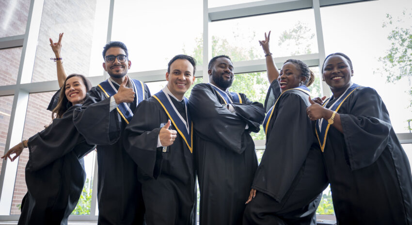 a group of six students wearing black graduation robes pose for a photo with her thumbs up and arms in the air