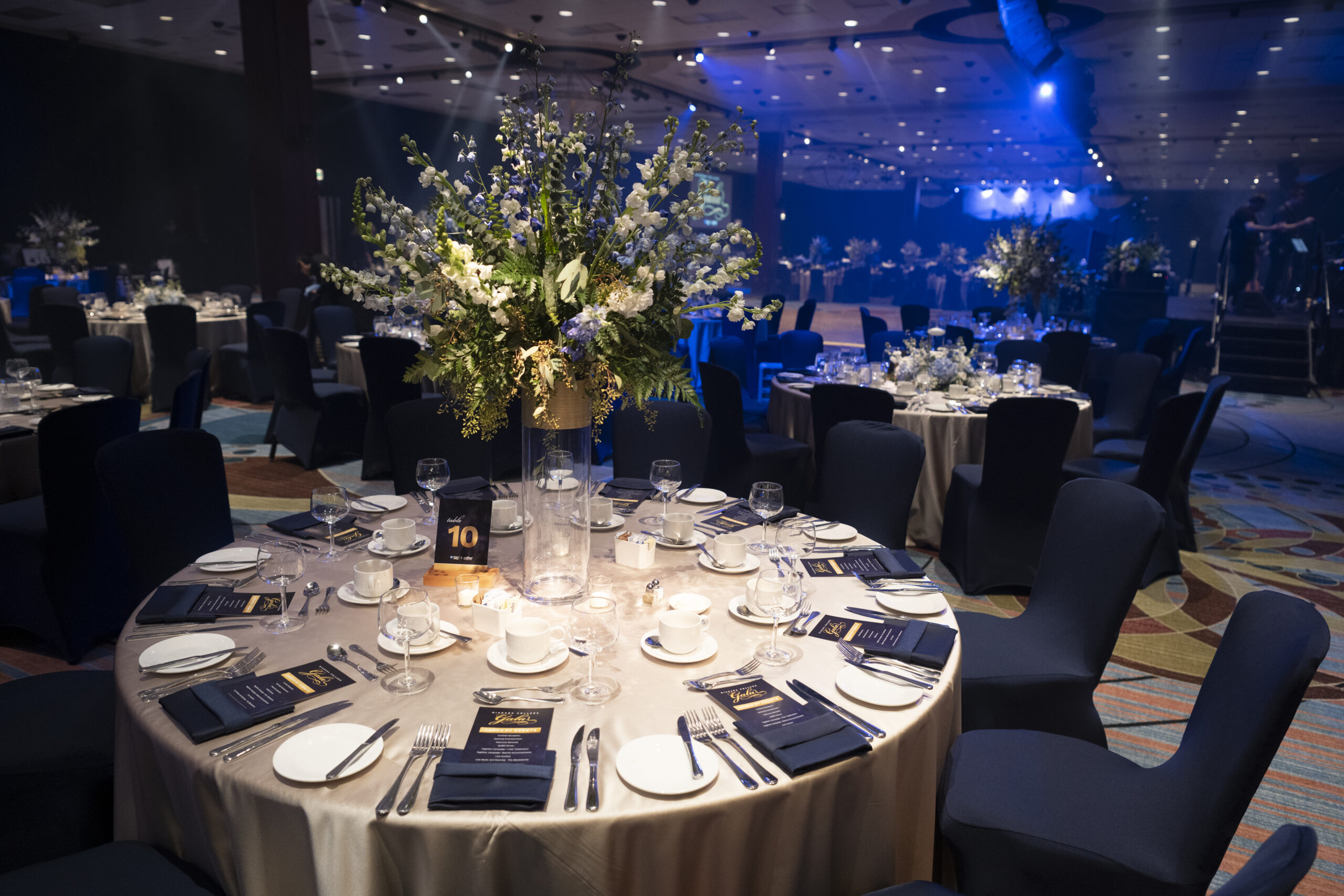 Elegant round tables set for gala event with central floral arrangement of blue and white flowers