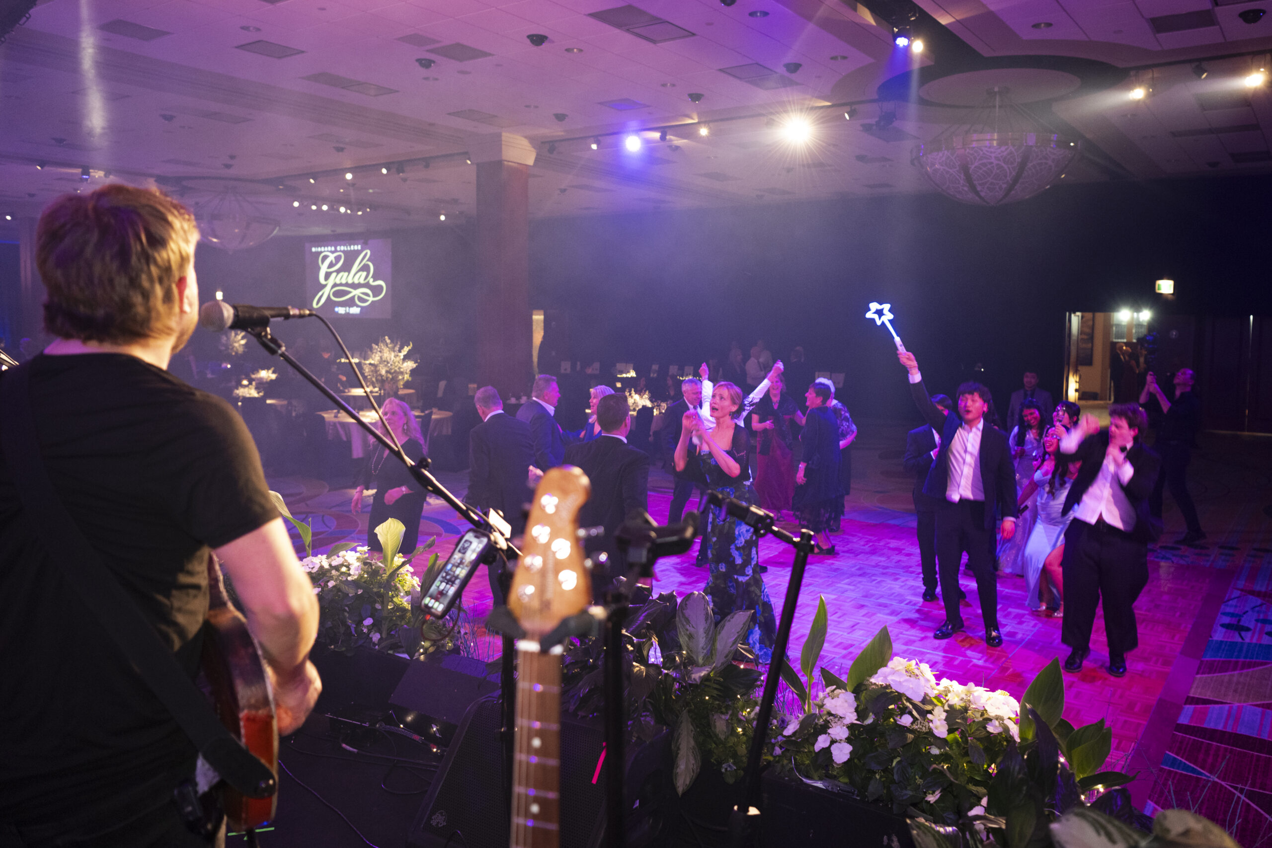 Musician performs on stage at a gala with attendees cheering and dancing.