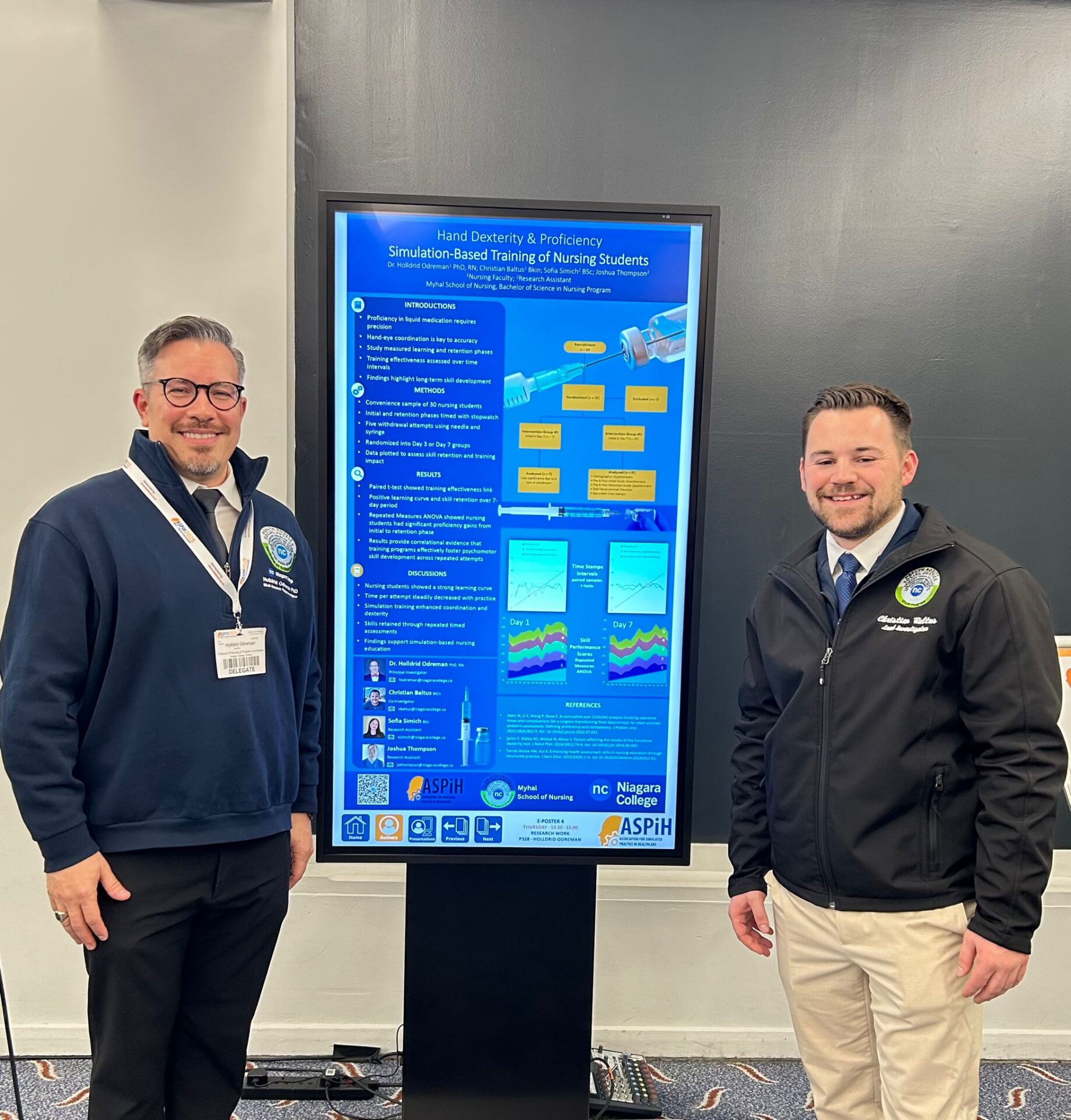 two men stand on either side of a vertical screen displaying a presentation graphic