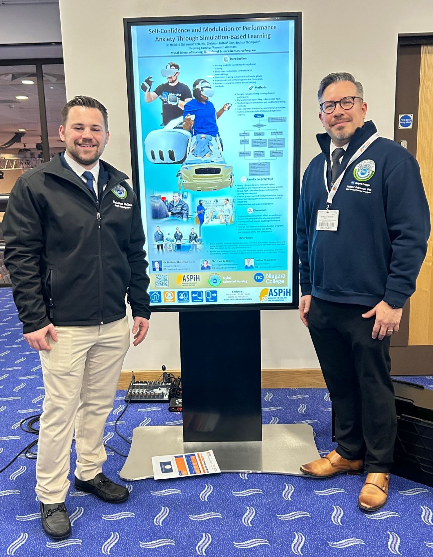 two men stand on either side of a vertical screen displaying a poster presentation graphic