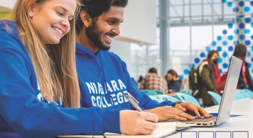 two students wearing blue Niagara College hoodies work at a table in a bright space
