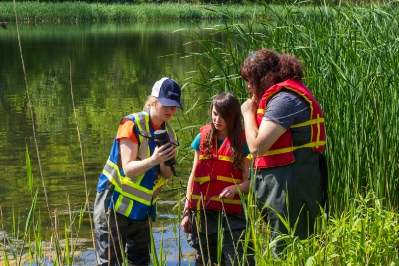 Colleen-showing-students-a-reading-on-water-quality-equipment.webp